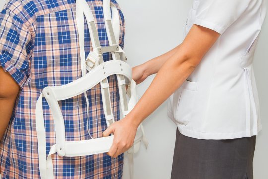 A doctor helping a patient who is suffering from scoliosis with how to wear a back brace.
