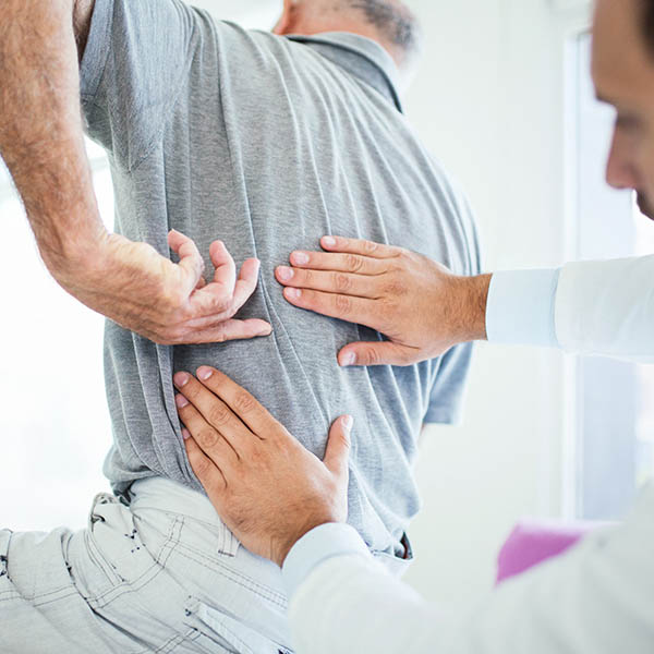 A doctor is performing non-surgical treatment on an old man who is suffering from back pain.