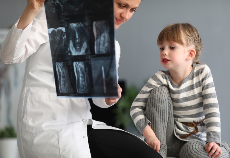 Doctor explaining pediatric spinal deformities treatment to a kid using an X-ray.
